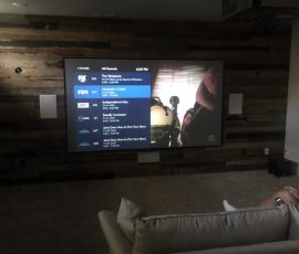 A large TV screen displays a channel guide and a show in a dimly lit living room with a couch in the foreground.