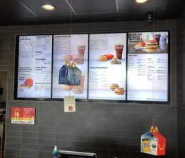 Digital McDonald's menu boards display various meal, breakfast, and drink options above a counter with registers.