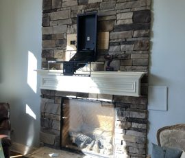 Stone fireplace with white mantel, wall-mounted TV bracket, tools, and sunlight streaming in from the left side.