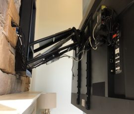 Flat-screen TV mounted on a wall with an adjustable swing arm bracket, showing cables and connection ports.