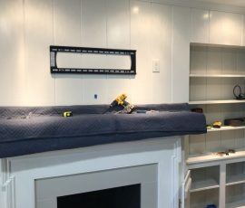 A TV wall mount is installed above a fireplace mantel, with tools and a padded cover on top of the mantel.