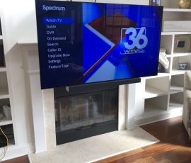 A flat-screen TV mounted above a fireplace displays a Spectrum menu and the 36 WTVQ news channel.