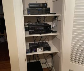 Electronics including a router, stereo receiver, and audio equipment are organized on shelves inside a closet.