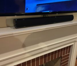A soundbar is positioned on a white mantel beneath a wall-mounted TV above a brick fireplace.