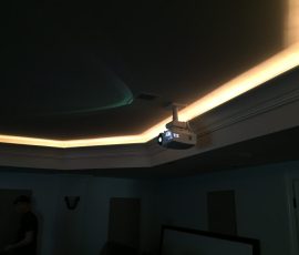Ceiling-mounted projector is turned on in a dimly lit room with recessed lighting along the ceiling edge.