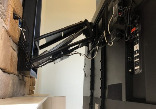 Flat-screen TV mounted on a retractable wall arm above a fireplace, with cables connected and visible brackets.
