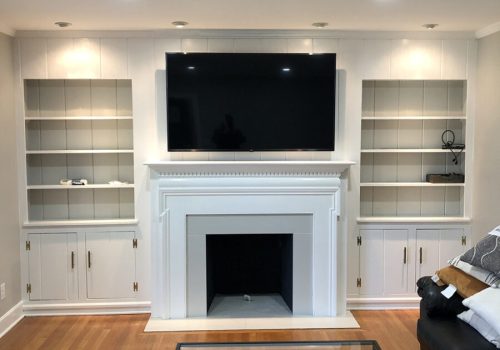 Living room with a wall-mounted TV above a white fireplace, built-in shelves, cabinets, and a glass coffee table.