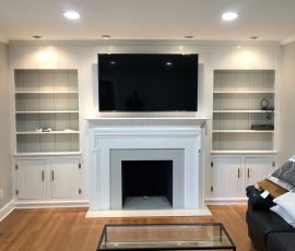 Living room with a wall-mounted TV above a white fireplace, built-in shelves, cabinets, and a glass coffee table.