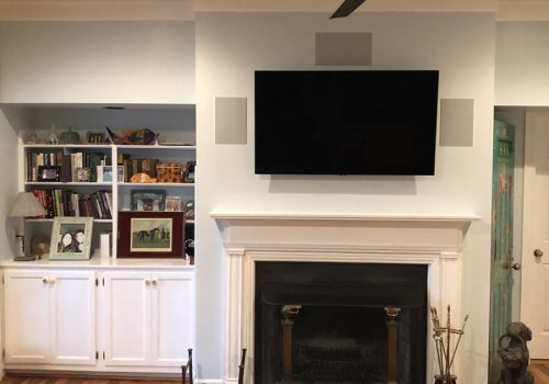 A living room with a wall-mounted TV above a fireplace, built-in shelves, and wooden floors.